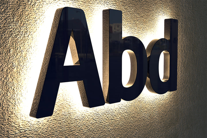 Custom black LED backlit sign Abd with warm white halo glow on textured wall.