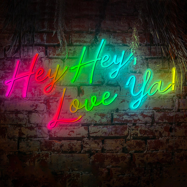 A vibrant multicolor neon LED sign displaying Hey Hey Love Ya mounted on a rustic brick wall