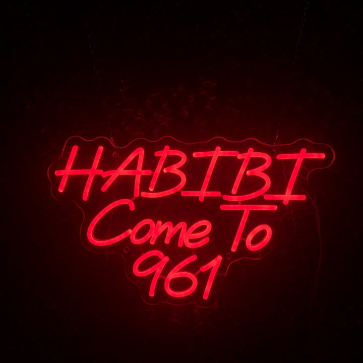 Red LED neon sign spelling out HABIBI Come To 961 against a dark wall