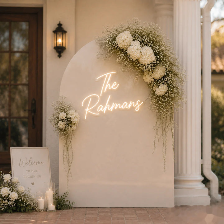 Wedding neon sign with “The Rahmans” custom surname lettering in warm white LED on acrylic backing for minimalist luxury wedding welcome backdrop decor.
