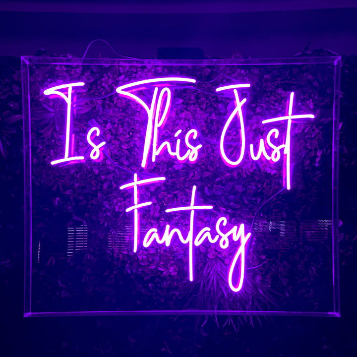 Vibrant purple LED neon sign displaying Is This Just Fantasy on a dark green plant wall