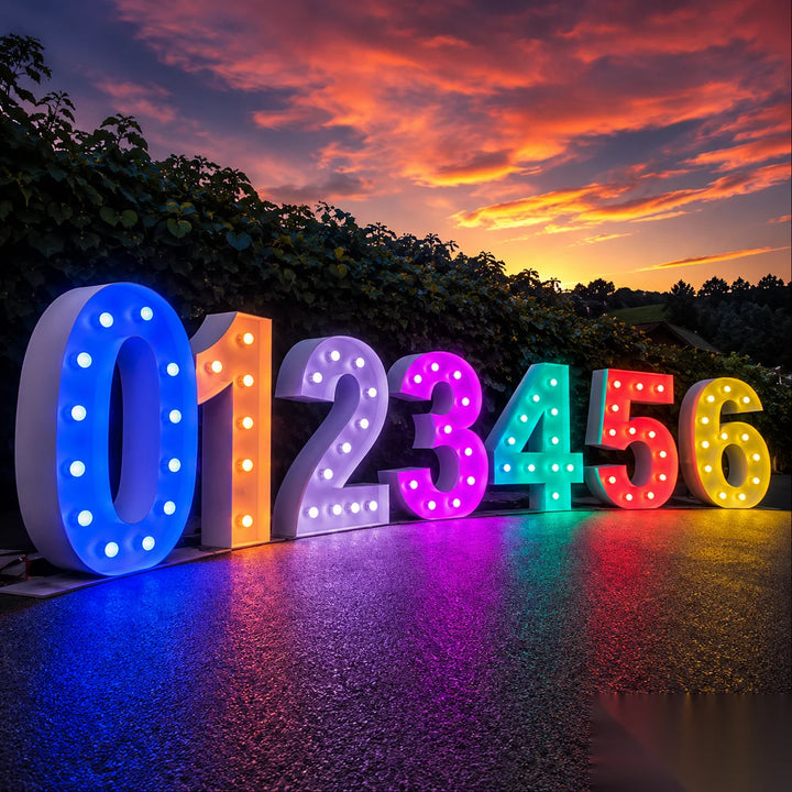 Oversized colorful marquee numbers 0 to 6 illuminated with LED bulbs at sunset, displayed outdoors with vibrant sky reflections, ideal for milestone celebrations, corporate events, birthdays, graduations, and custom event signage.