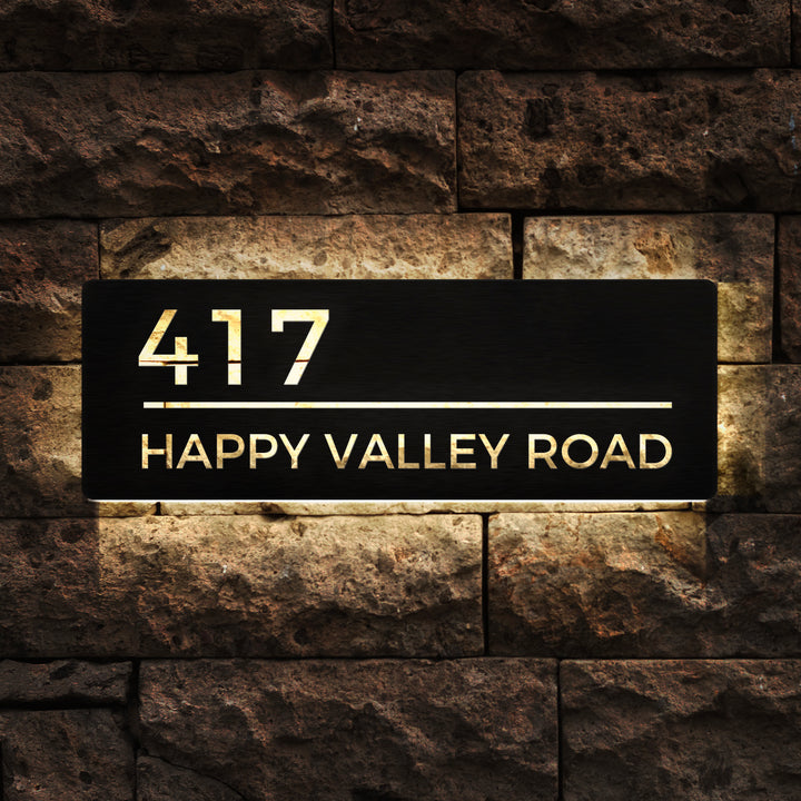 Custom black LED backlit address sign displaying 417 Happy Valley Road on a stone wall.