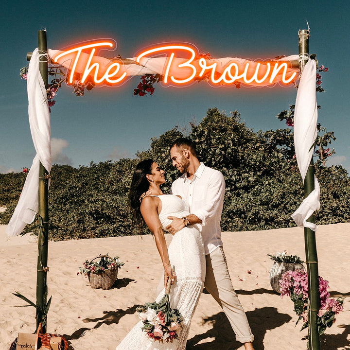 Custom orange neon LED sign spelling The Brown on a beach wedding arch.