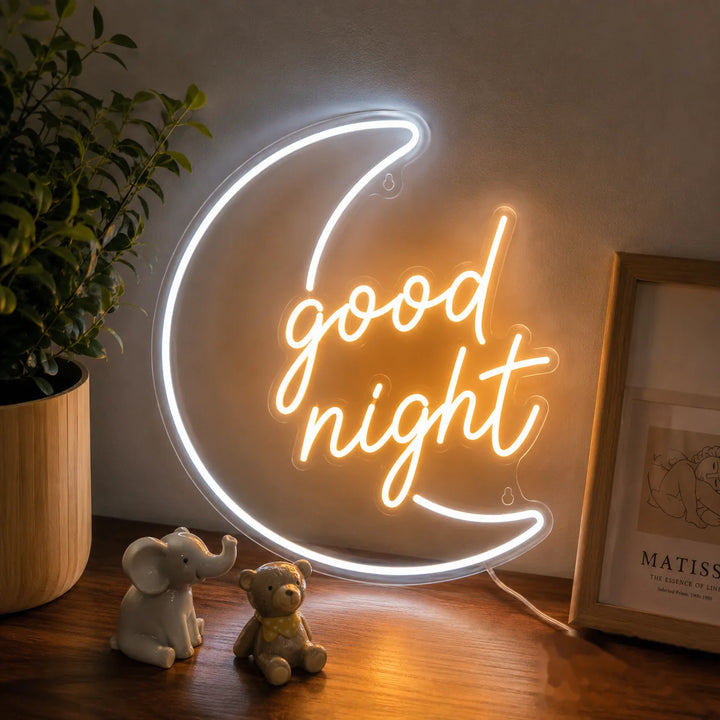 Crescent moon “good night” LED neon sign glowing on a wooden table in a cozy nursery or bedroom with warm ambient lighting and cute decor accents.
