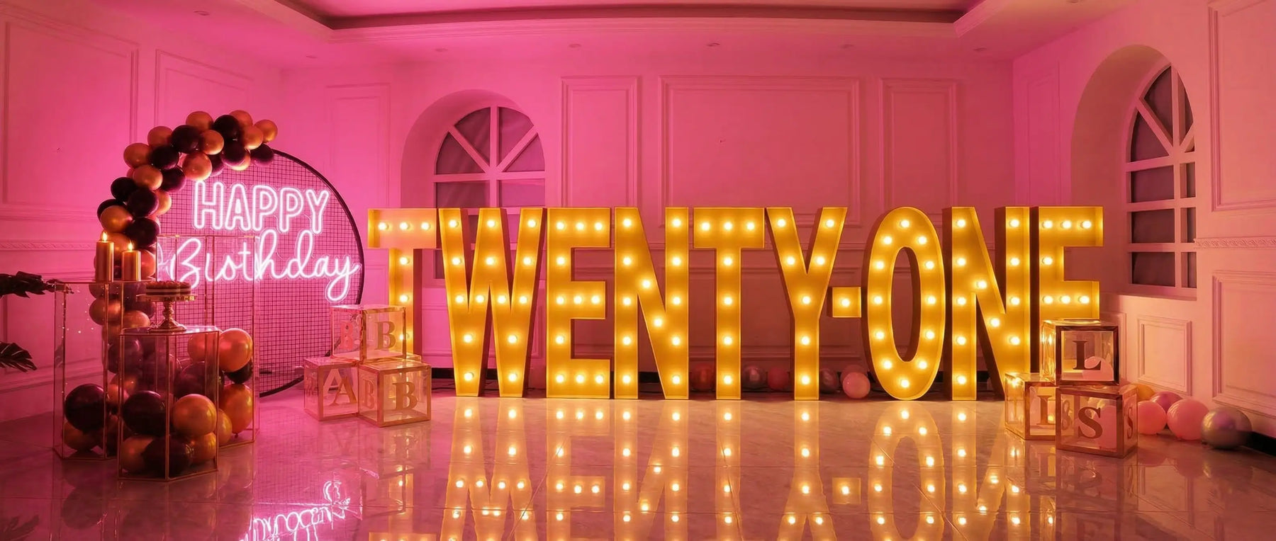 Decorative setup with 'Happy Birthday' and 'TWENTY-ONE' lights in a room with pink walls.