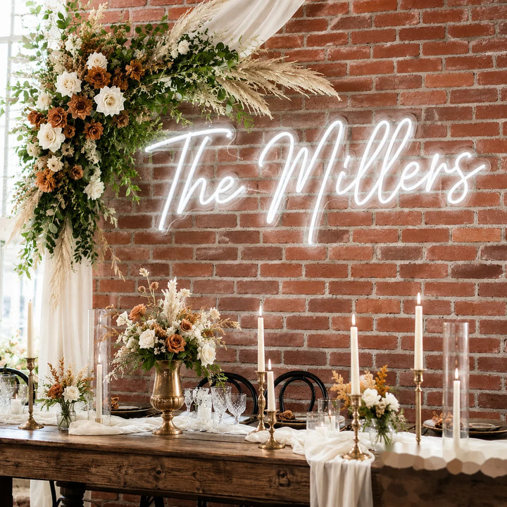 Wedding neon sign with “The Millers” surname lettering in warm white LED on clear acrylic backing for rustic industrial wedding reception backdrop decor.